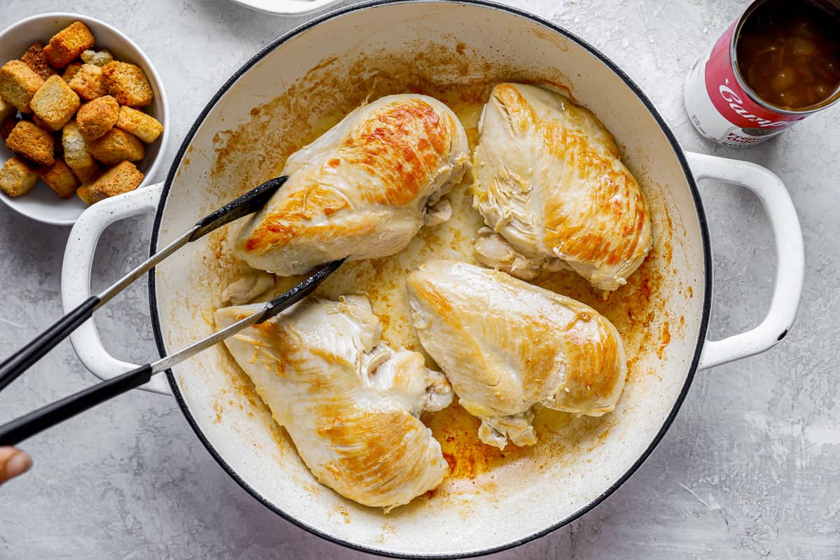 4 seared chicken breasts in a pan with tongs.