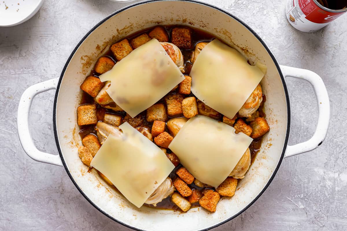 Cheese slices on top of chicken breasts in a pan with croutons.