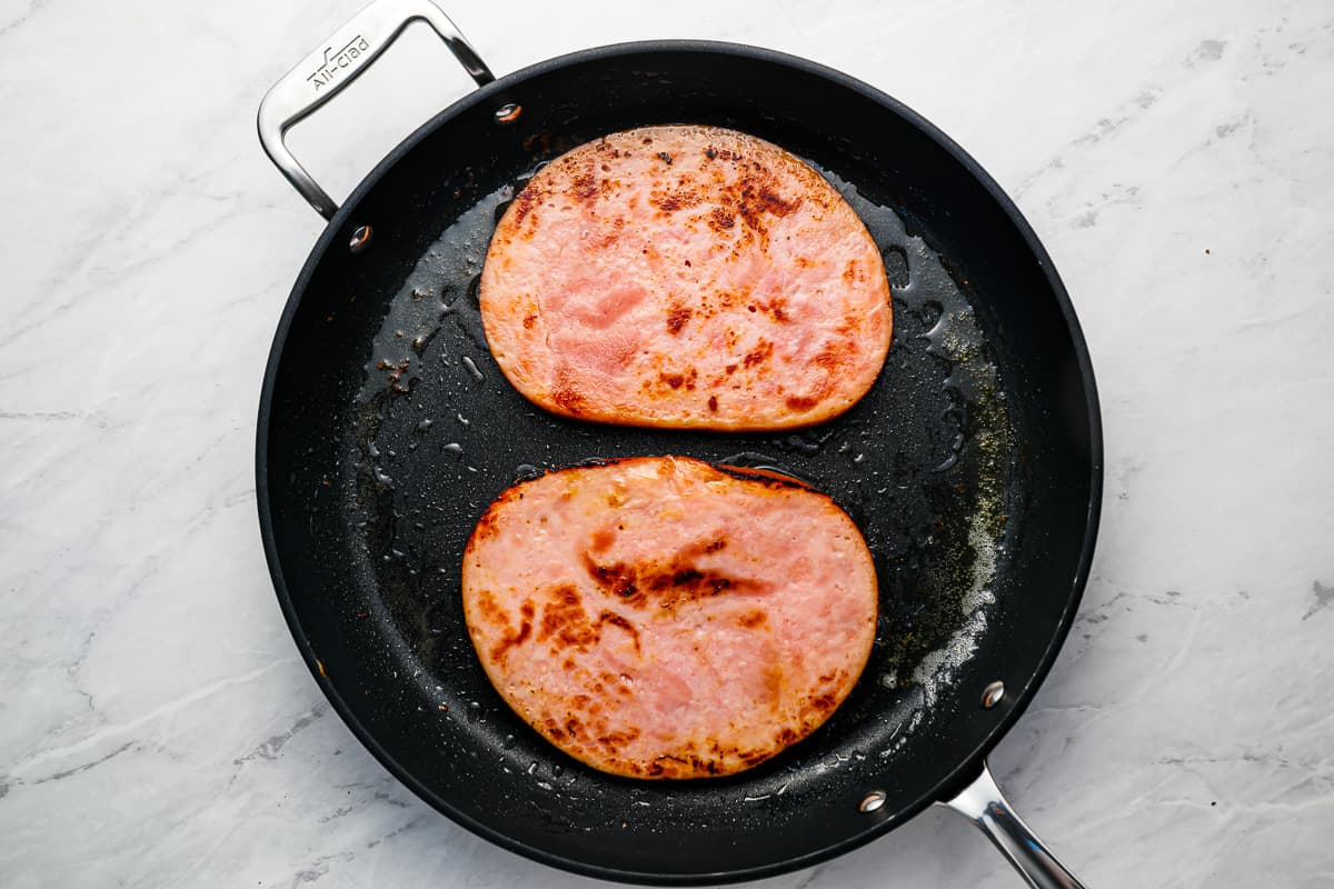 Two pieces of ham being cooked in a pan.