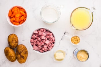 Ham, carrots, potatoes and other ingredients on a white marble table.