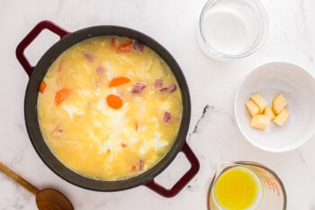 A pot of soup with carrots, onions and ham.