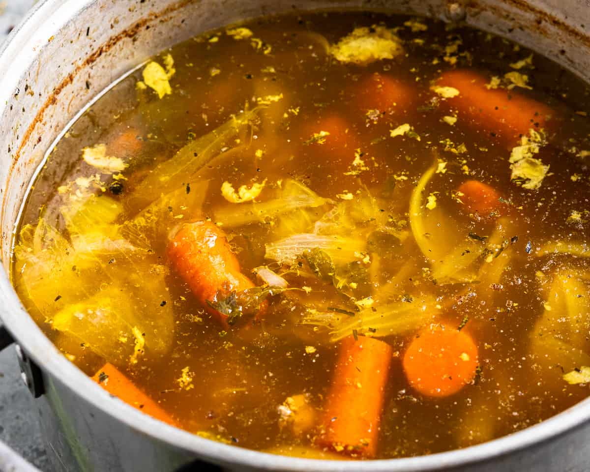 A pot of chicken soup with carrots and onions.