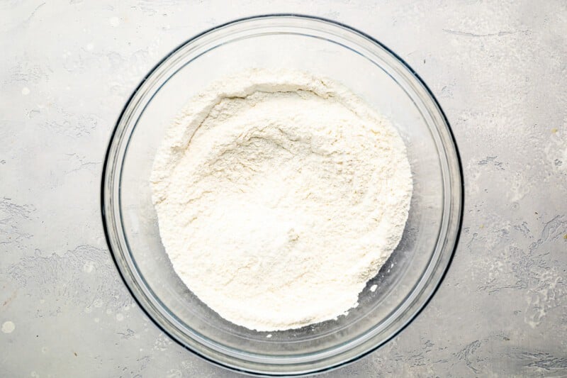 White flour in a glass bowl on a gray surface.