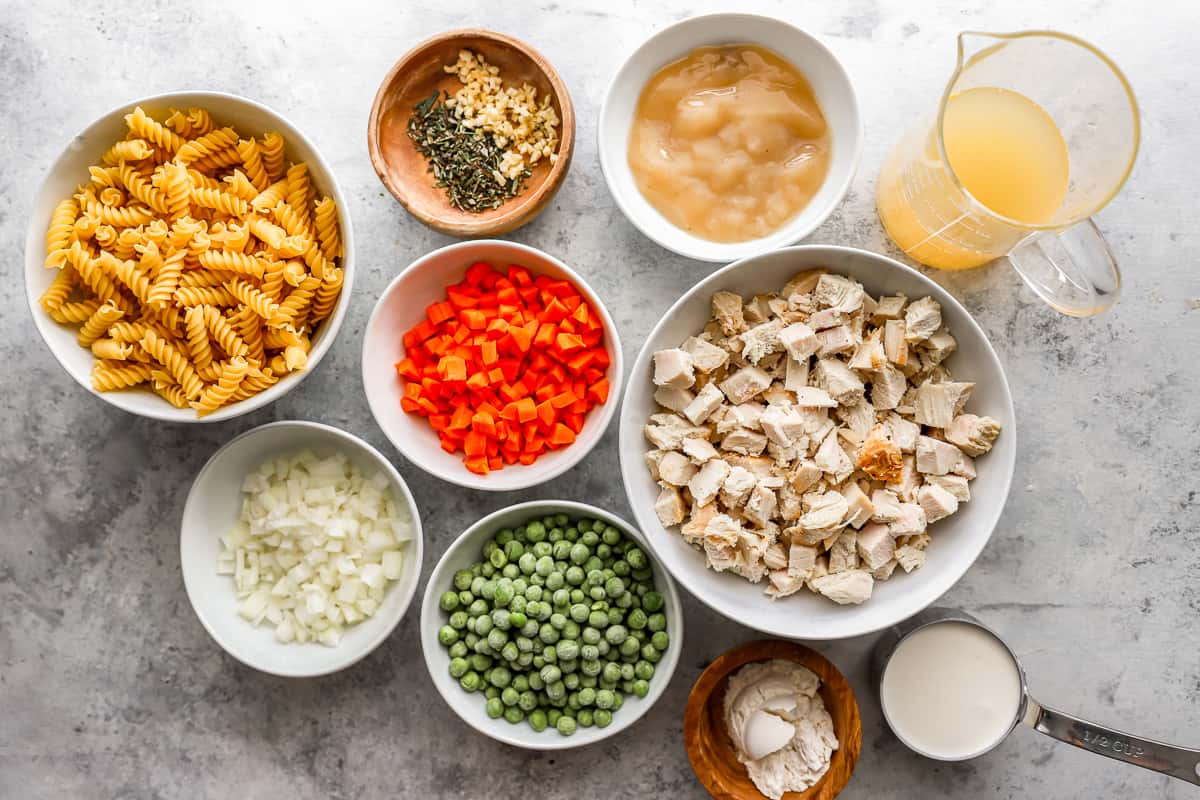 A bowl of pasta, chicken, peas, carrots and other ingredients.