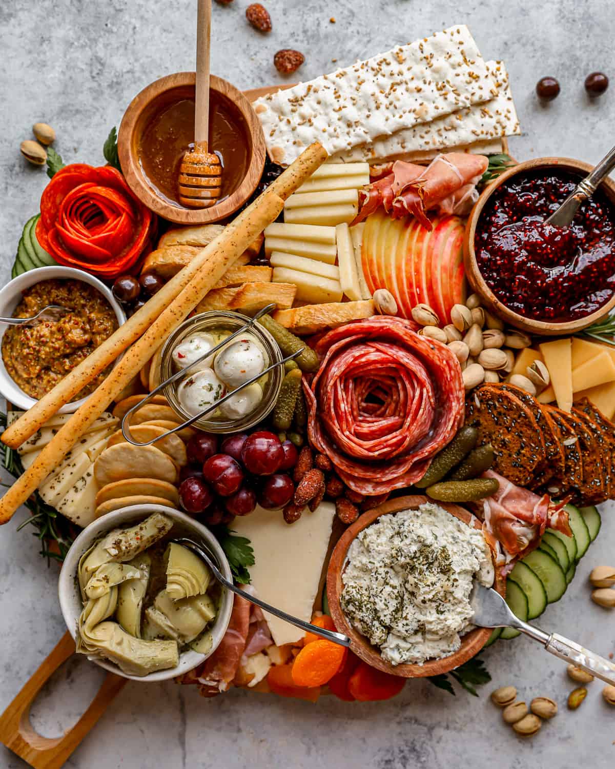 Overhead view of a beautiful charcuterie board, filled with a variety of meats and cheeses, crackers, dips and spreads, vegetables and fruits, nuts, and more.