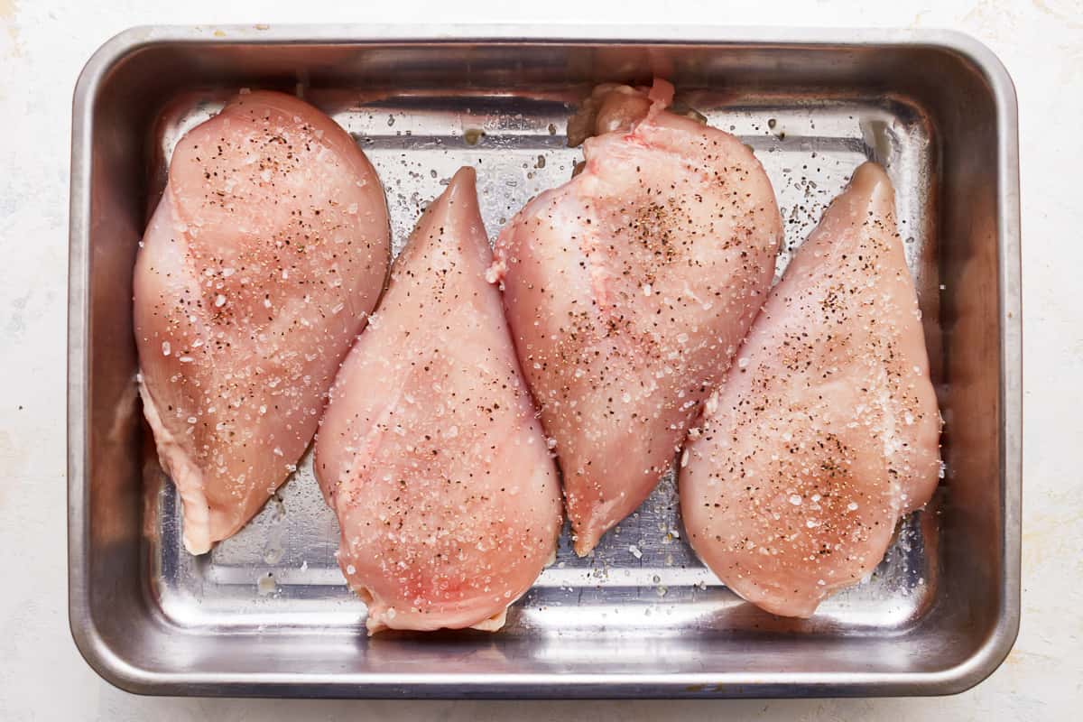 Seasoned chicken breasts in a pan.