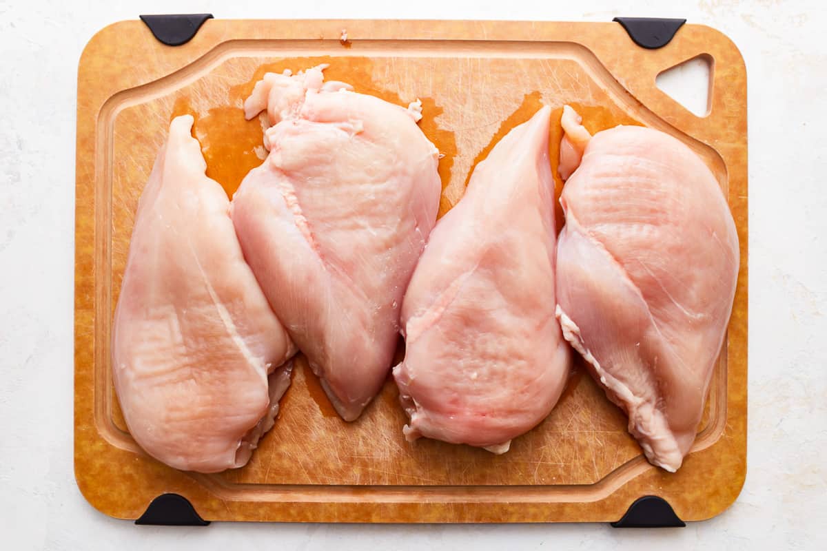 Chicken breasts on a wooden cutting board.
