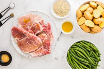Meat, potatoes, green beans and other ingredients on a white table.