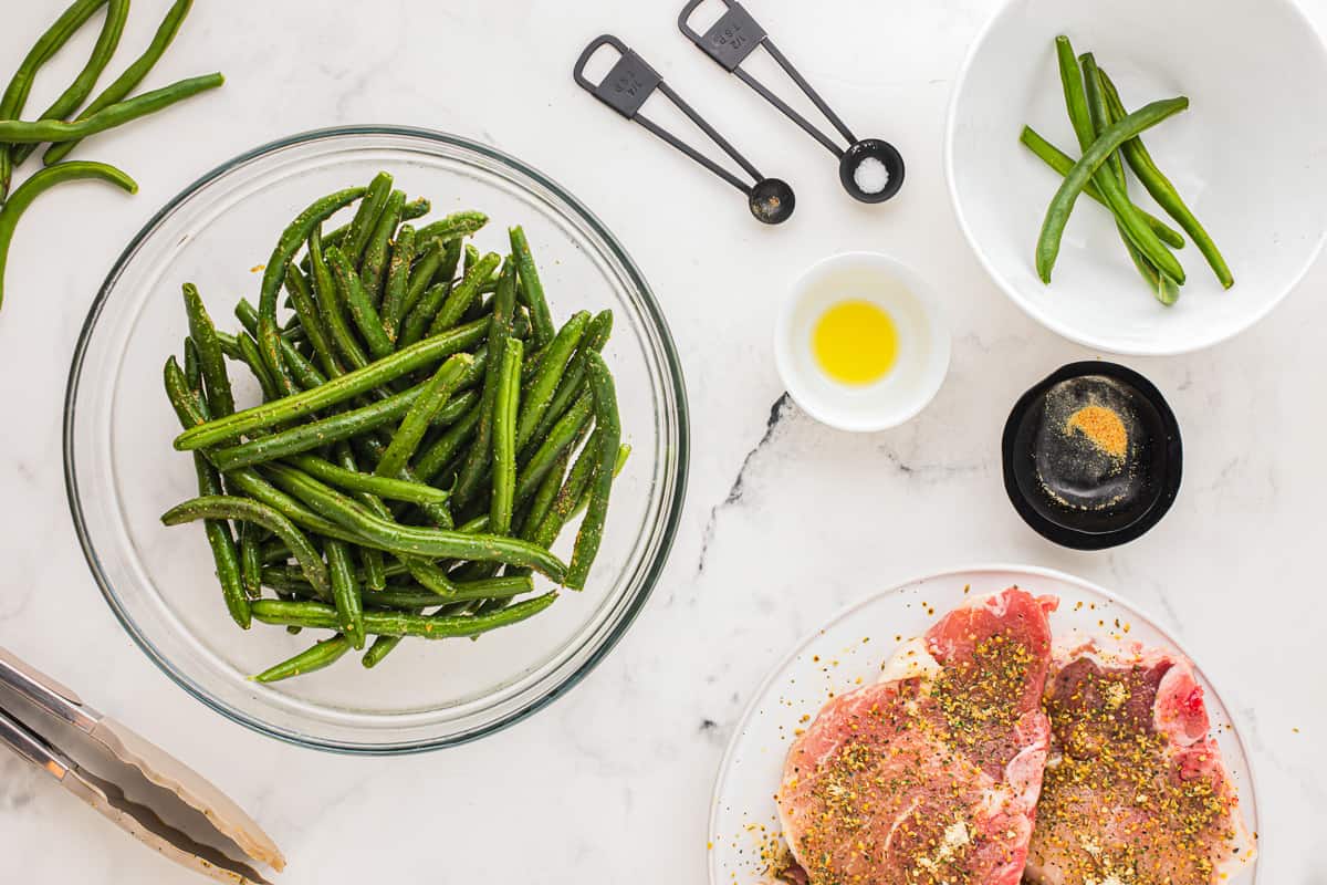 A bowl of green beans and meat on a marble table.