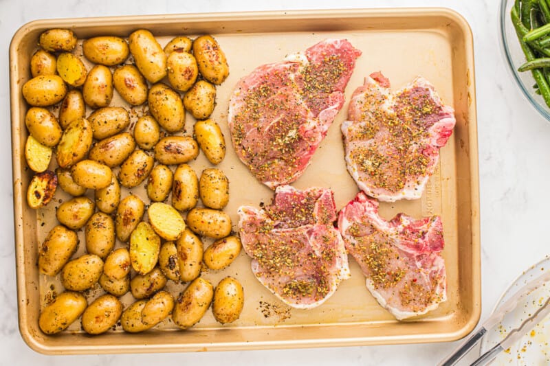 A baking sheet with meat, potatoes and green beans.