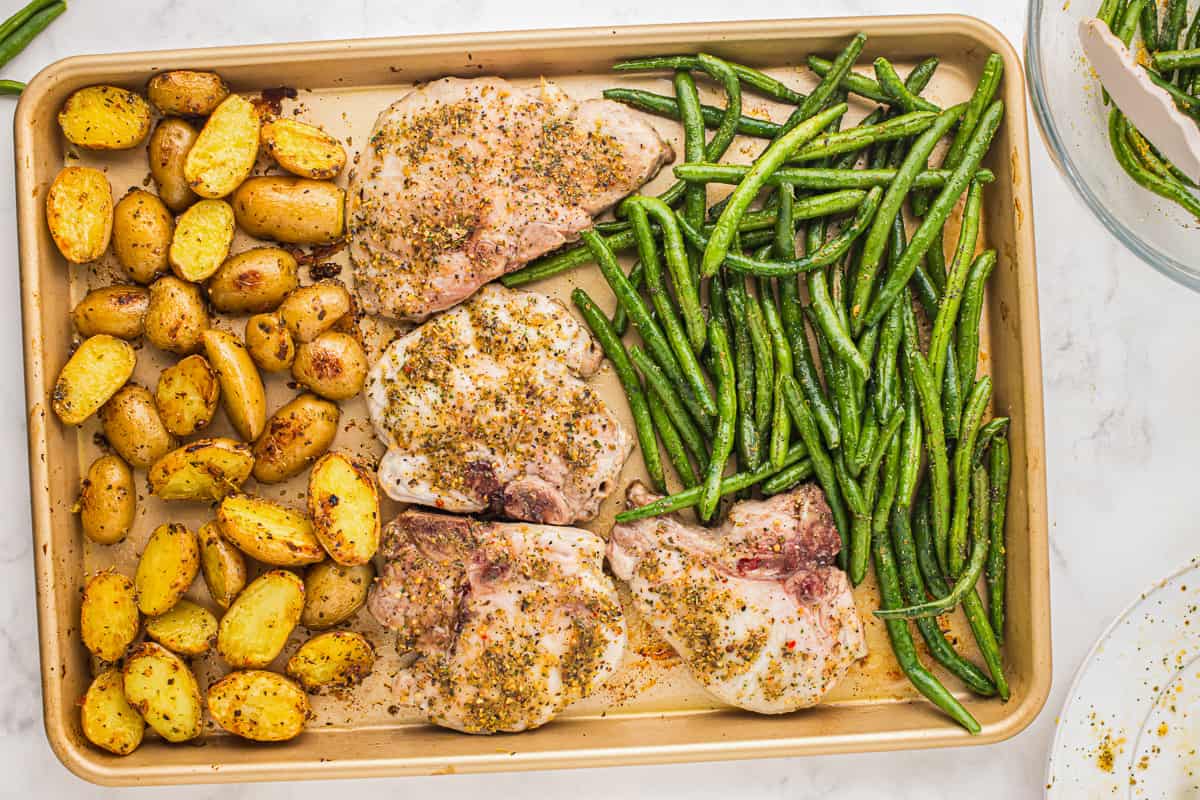 A sheet pan with pork chops, green beans, and potatoes.