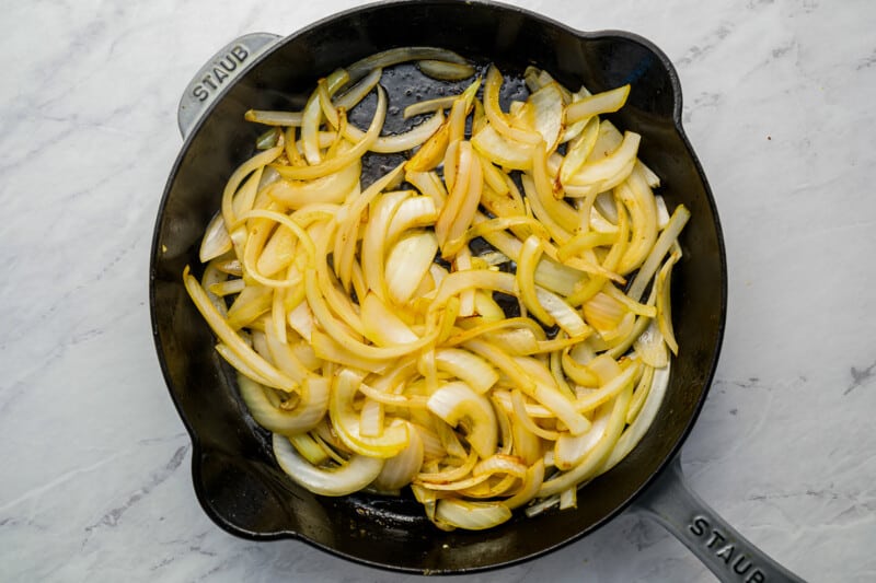 Sliced onions in a skillet on a marble countertop.