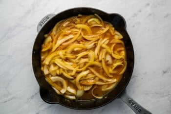 A skillet filled with onions and sauce.