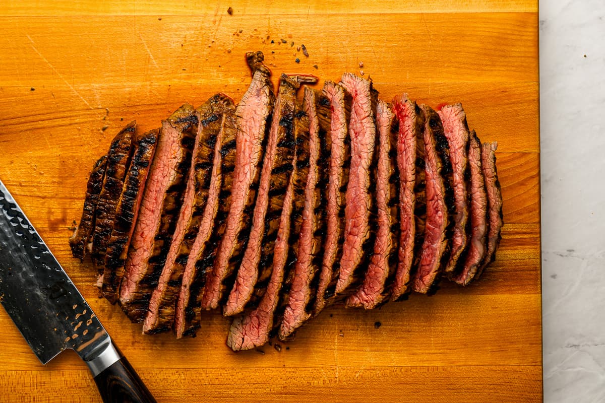 Grilled steak on a cutting board, cut into thin strips.