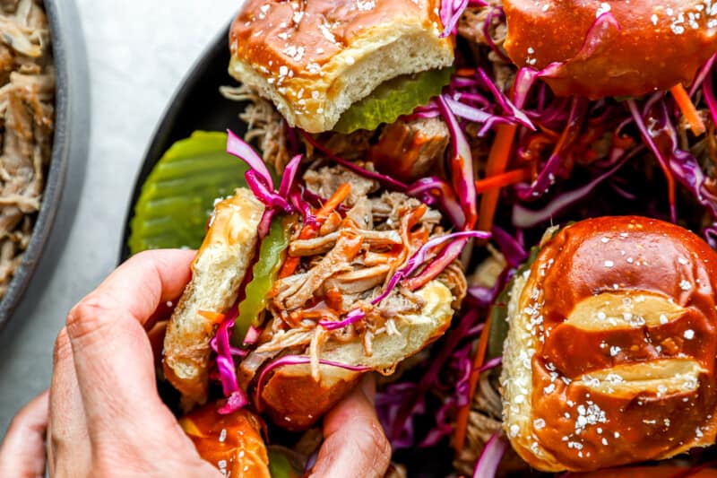 A person is holding a plate of pulled pork sliders.