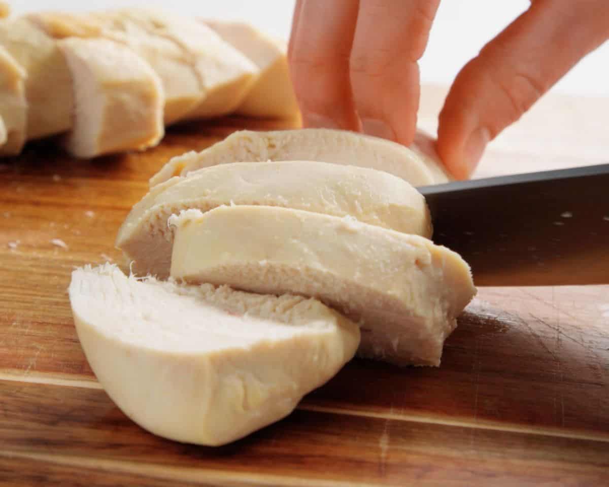 Sliced poached chicken breast on a cutting board showing juicy, tender texture