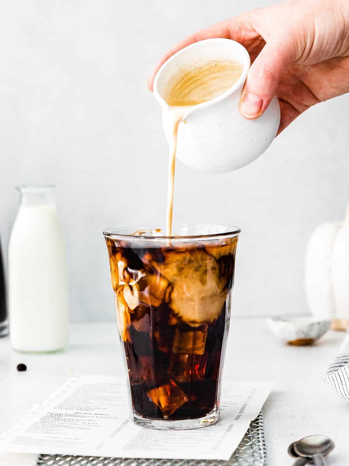 hand pouring pumpkin cold foam on top of a glass of cold brew.