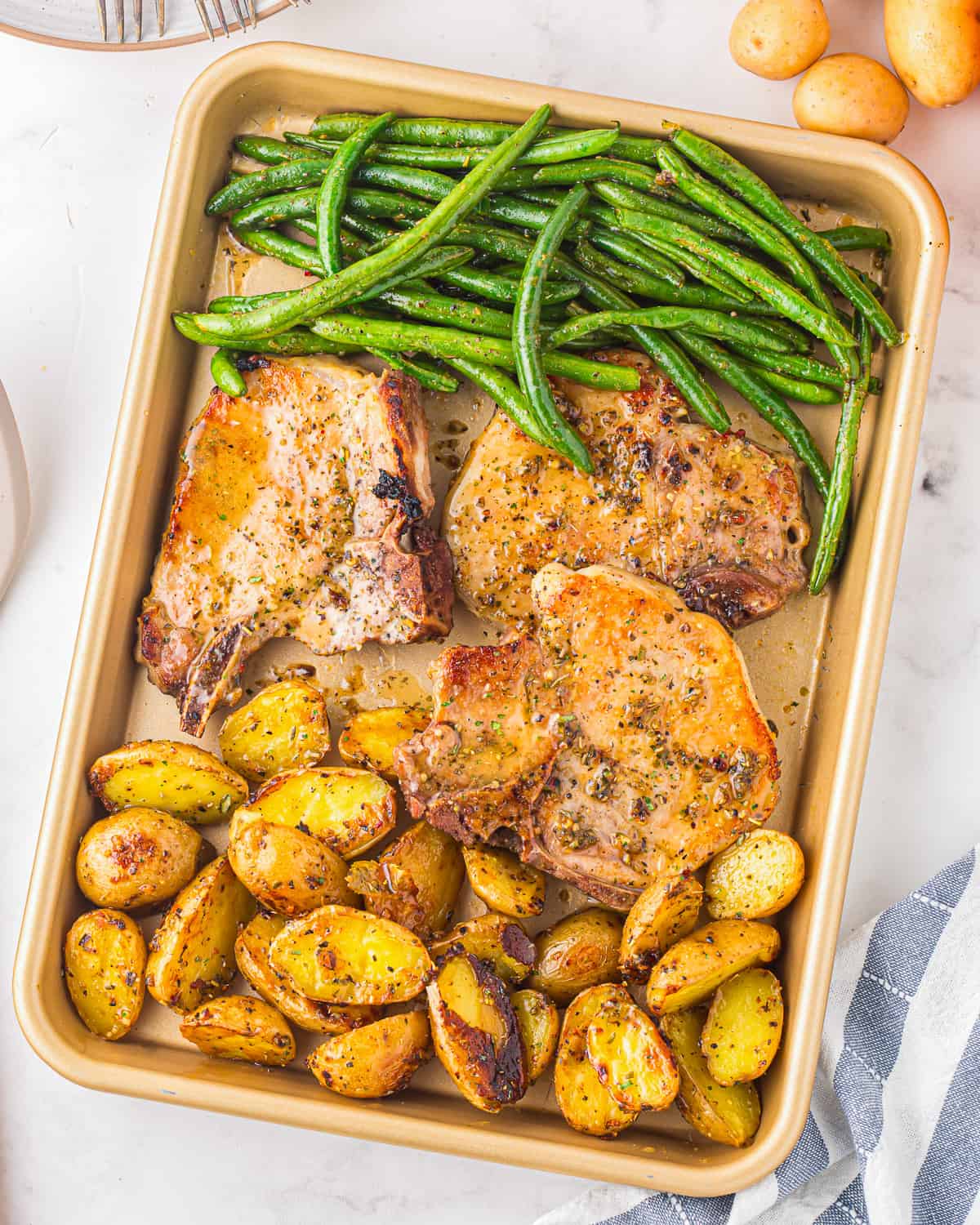 A sheet pan dinner with pork chops, potatoes, and green beans.