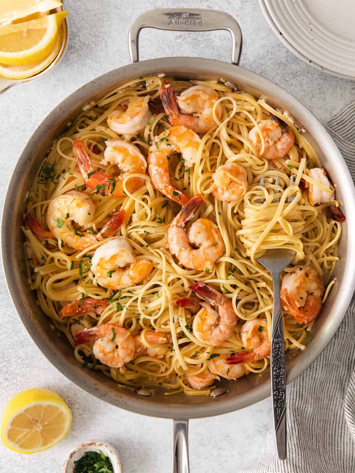 overhead view of pasta twirled around a slotted spoon resting on garlic shrimp scampi in a frying pan.