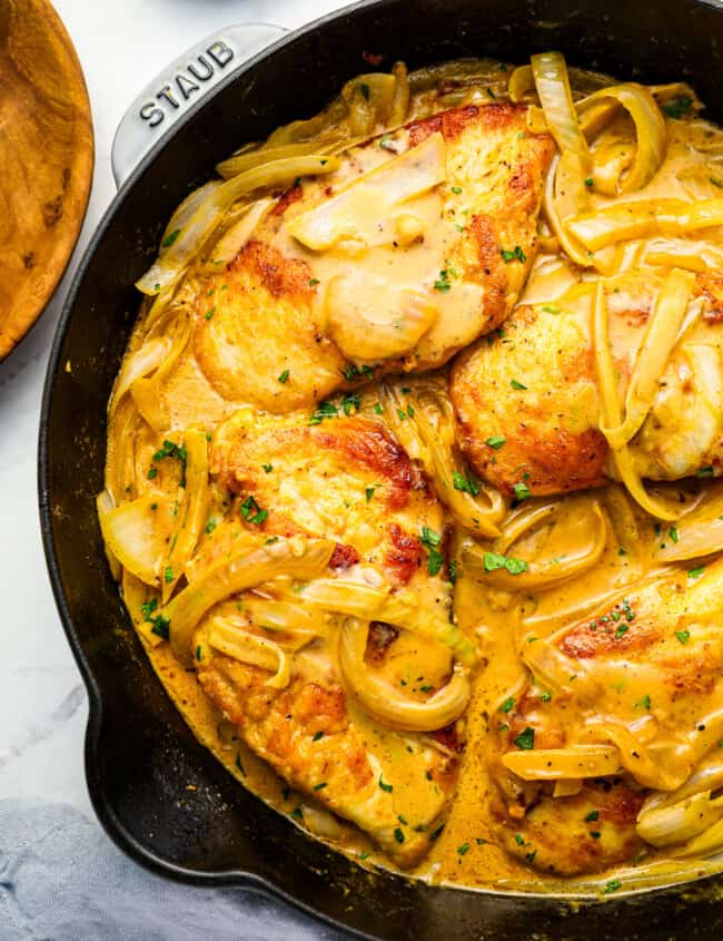 A skillet with chicken and onions in a sauce.