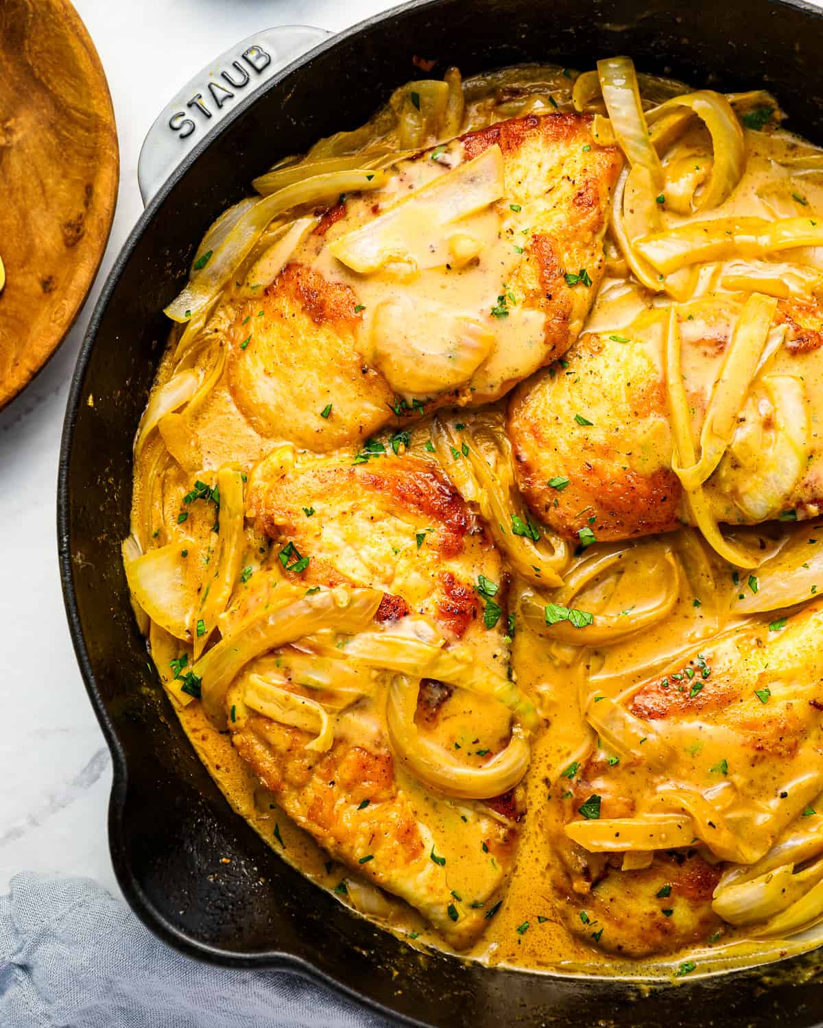 smothered chicken breast in a skillet with gravy and onions.