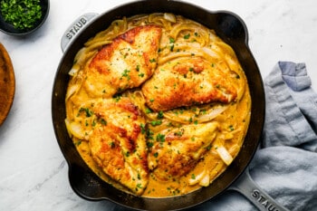 A skillet with chicken and onions in it.