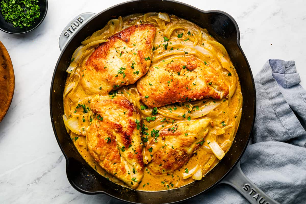 A skillet with chicken breast, gravy, and onions in it.