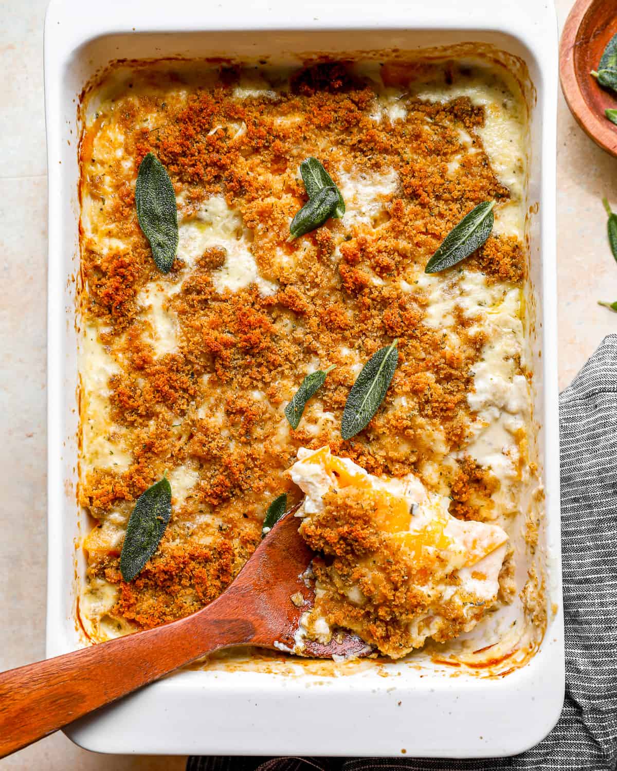 squash casserole with a wooden spoon and sage sprigs.