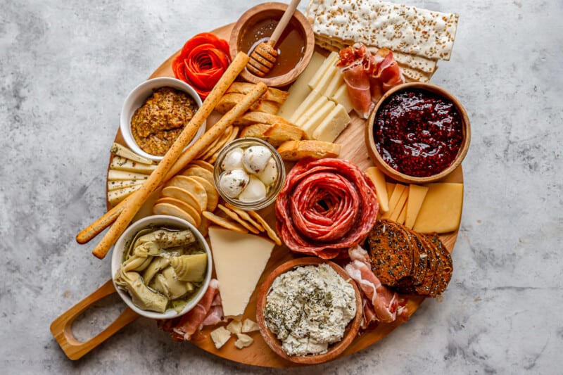 A wooden board with a variety of meats and cheeses.