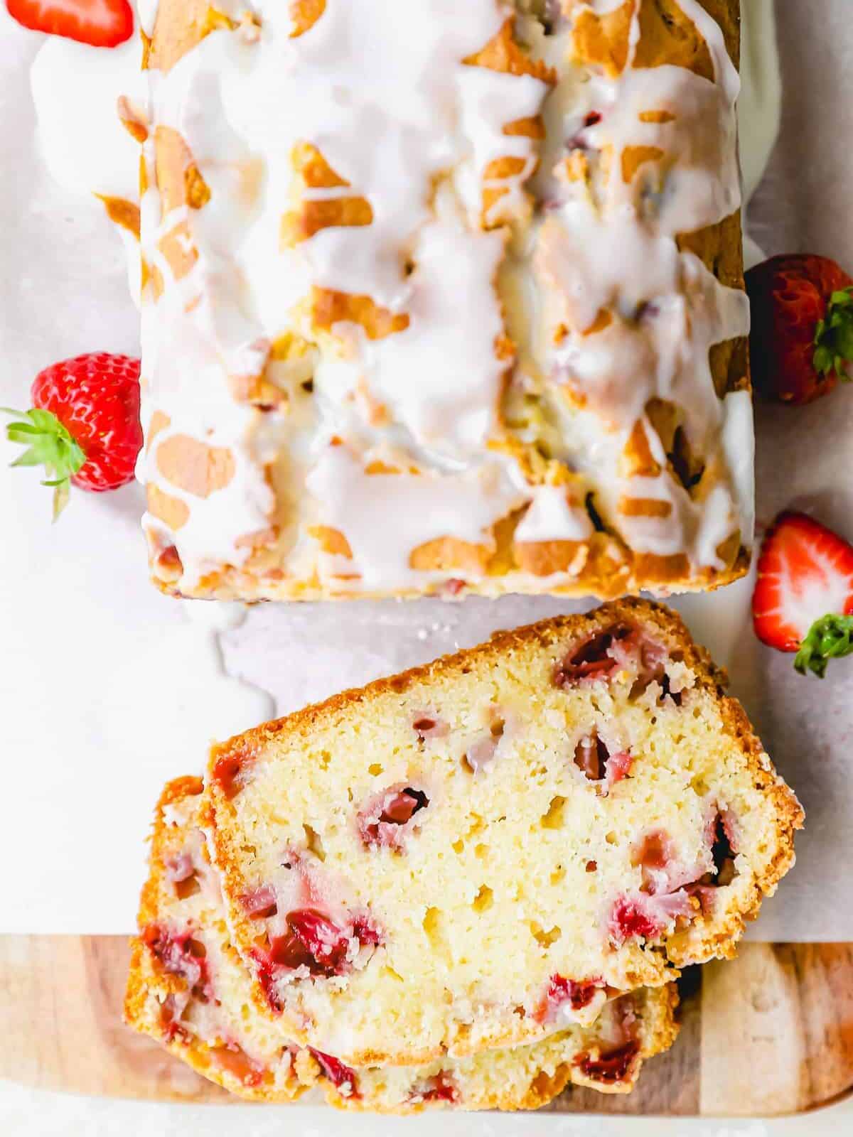 overhead view of sliced strawberry bread on parchment paper on a wooden cutting board with the slice facing up to show the interior texture.