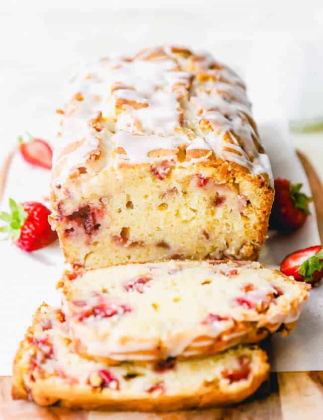 three-quarters view of sliced strawberry bread on parchment paper on a wooden cutting board with two slices laying in front of it.