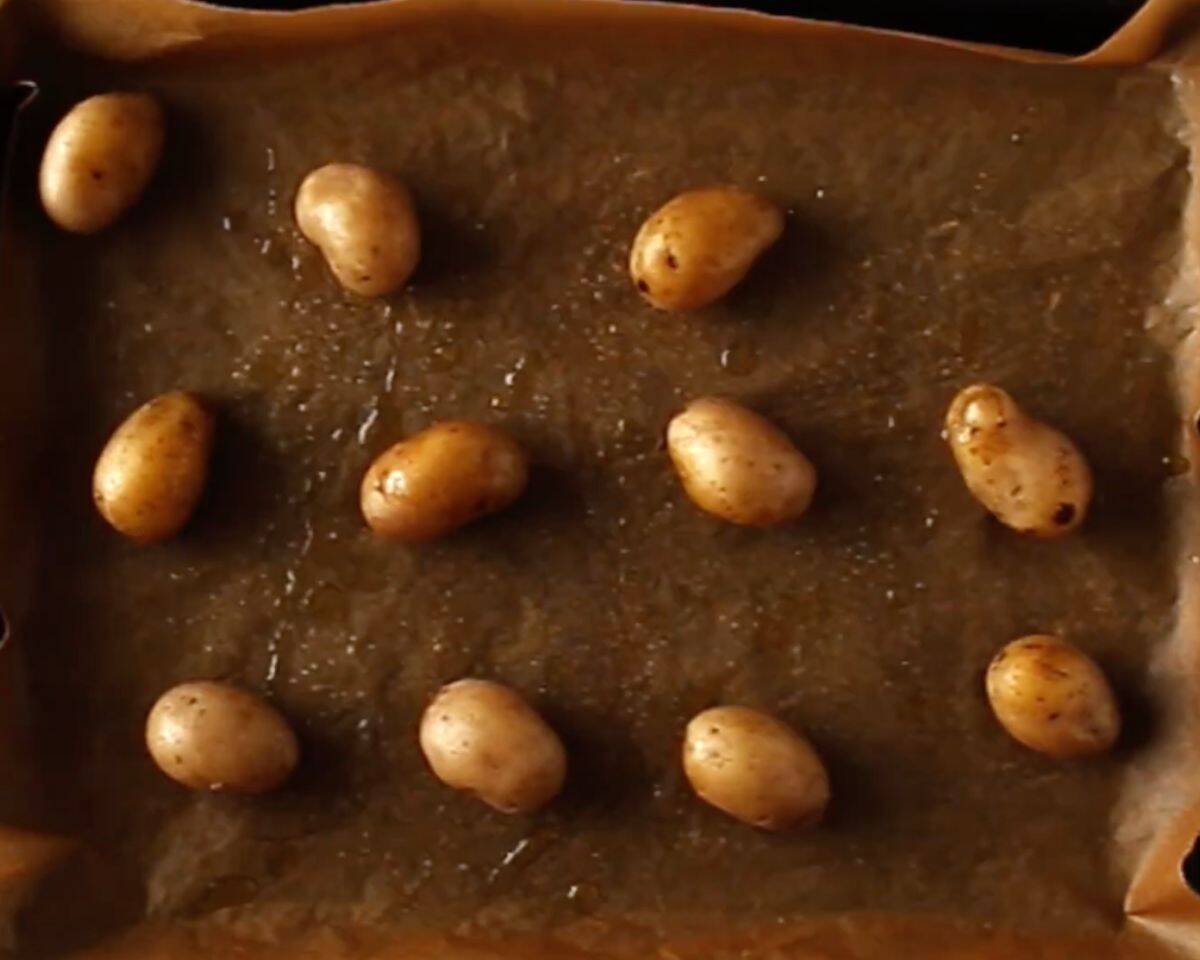 Par cooked baby potatoes spaced out on a parchment-lined baking sheet with olive oil. - 6