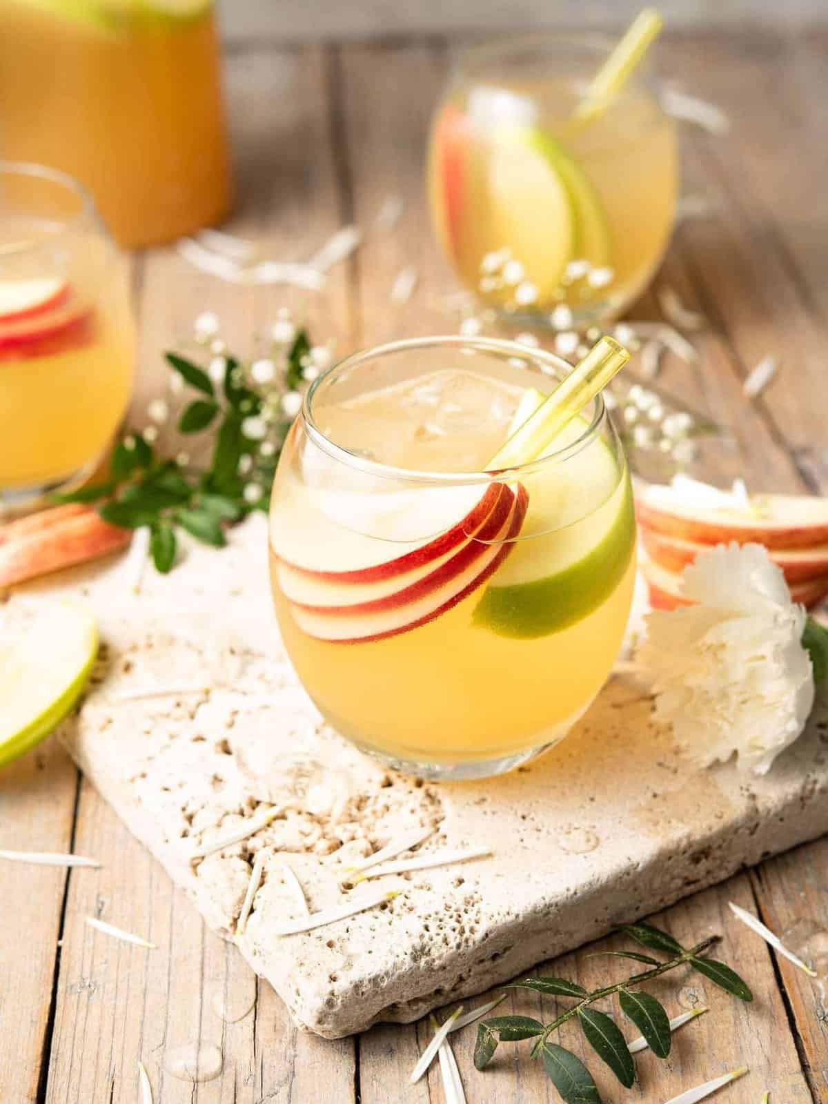 An apple pie-inspired drink, consisting of a pitcher of apple sangria garnished with slices of apples.