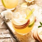 A refreshing apple pie drink garnished with slices of apples and sprigs of thyme.