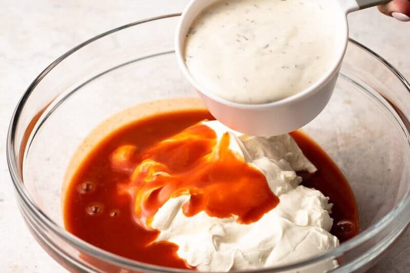 A person pouring buffalo chicken dip sauce into a bowl.