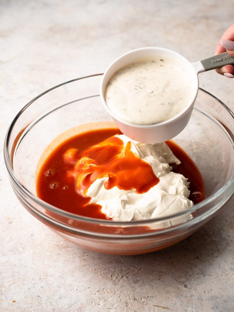 pouring ranch dressing into a mixing bowl with buffalo sauce and cream cheese.