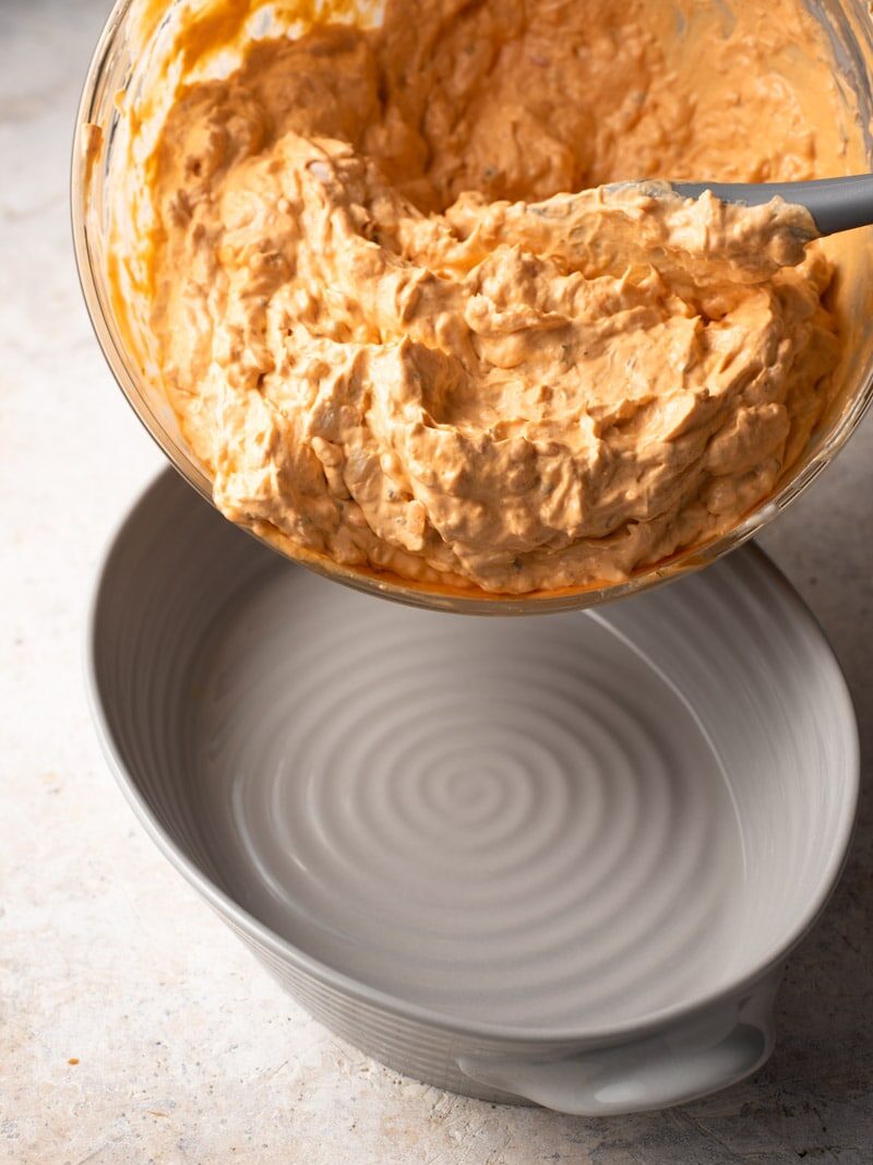 pouring buffalo chicken dip into a casserole dish.
