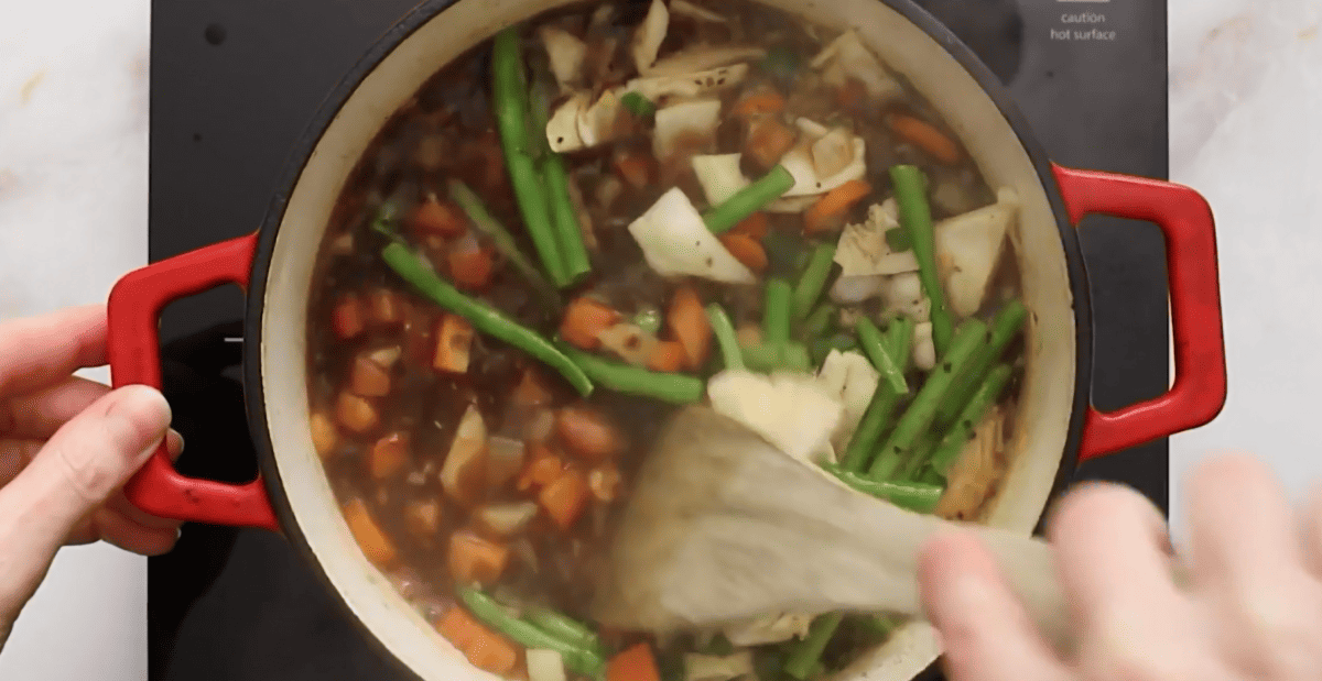 Adding vegetables, broth, tomato paste and cabbage to the soup pot. 