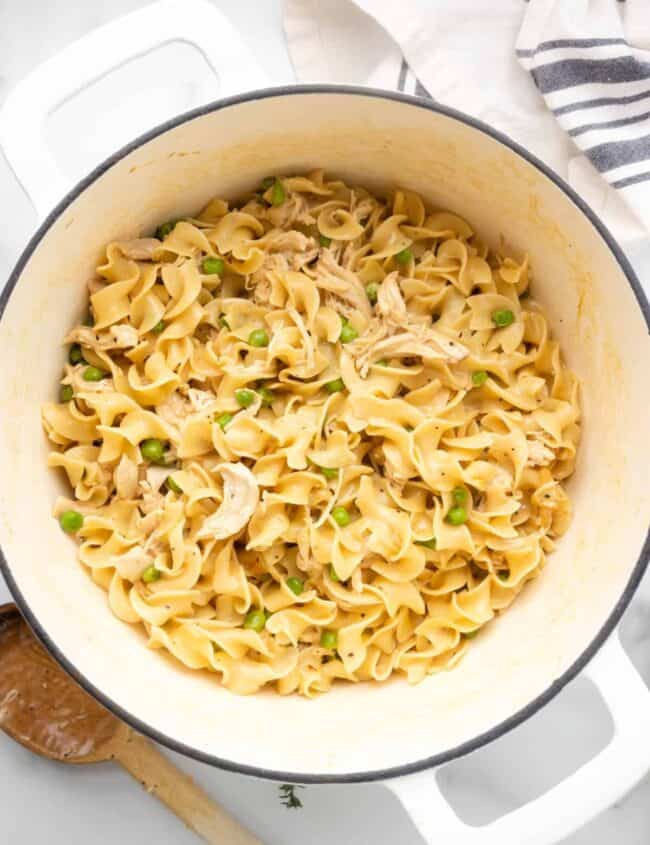 close-up overhead view of chicken and noodles in a white dutch oven.