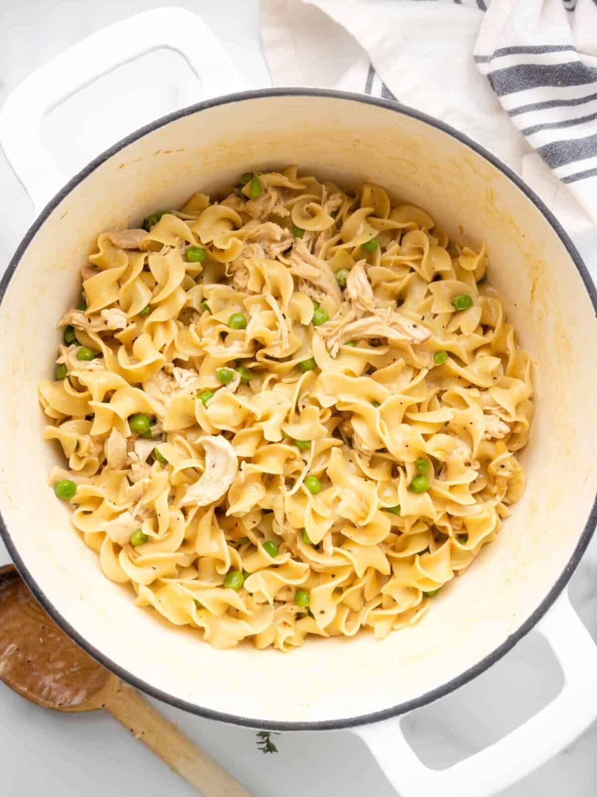 close-up overhead view of chicken and noodles in a white dutch oven.