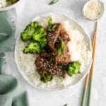 overhead view of instant pot mongolian beef over rice on a white plate with chopsticks.