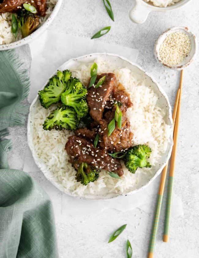 overhead view of instant pot mongolian beef over rice on a white plate with chopsticks.