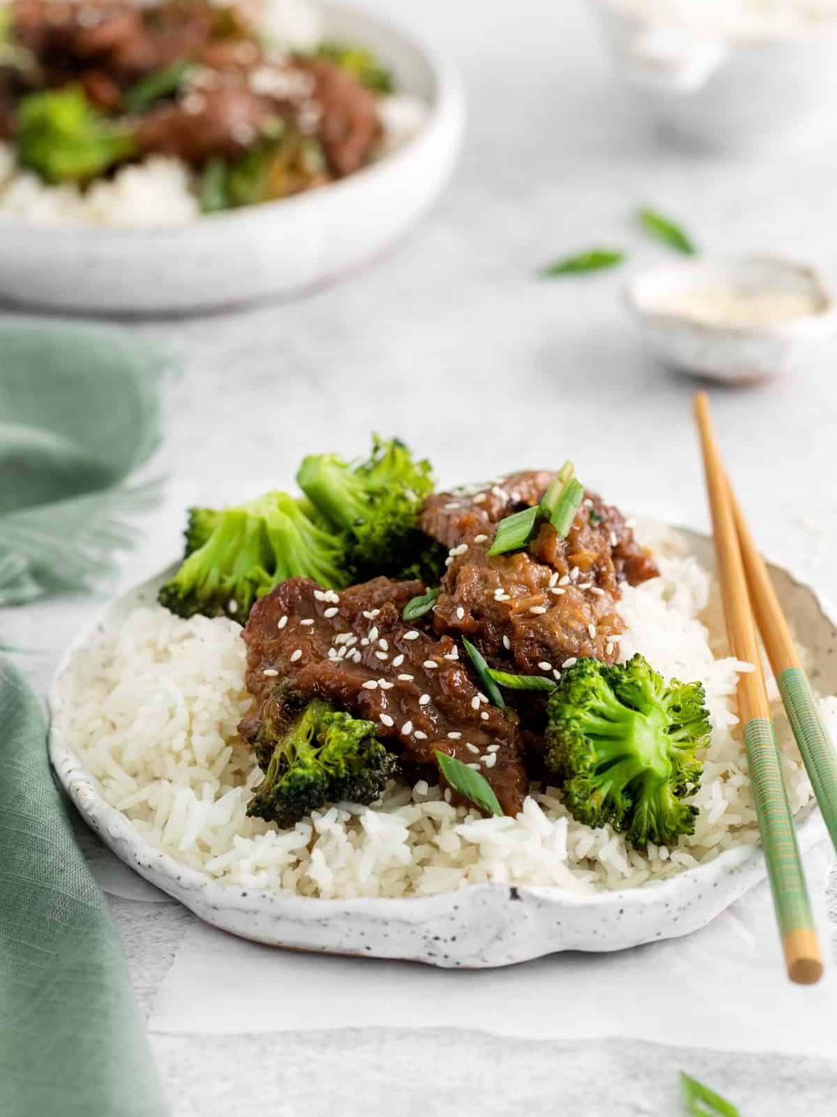 instant pot mongolian beef over rice on a white plate with chopsticks.