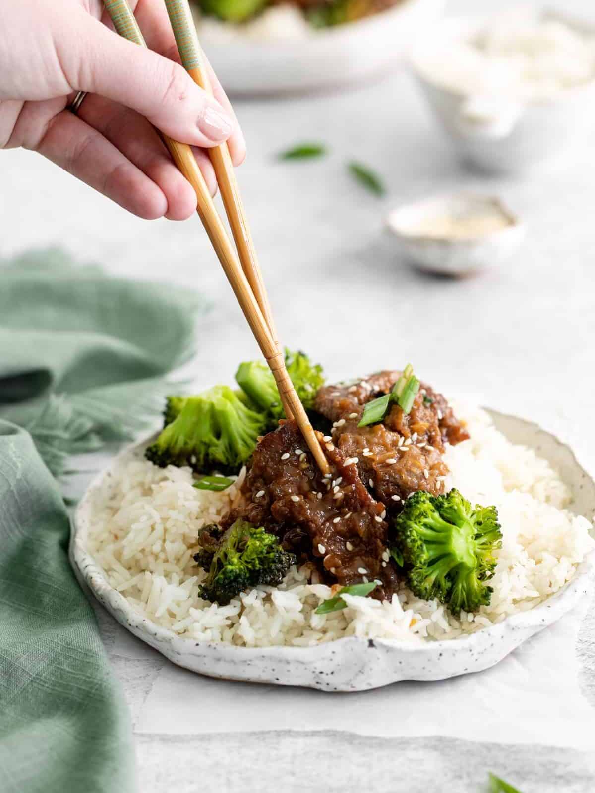 a hand using chopsticks to grab a piece of instant pot mongolian beef from a white plate.