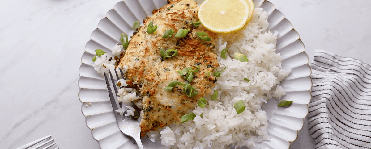 Tilapia on a plate with green onions, lemon slices and white rice. 