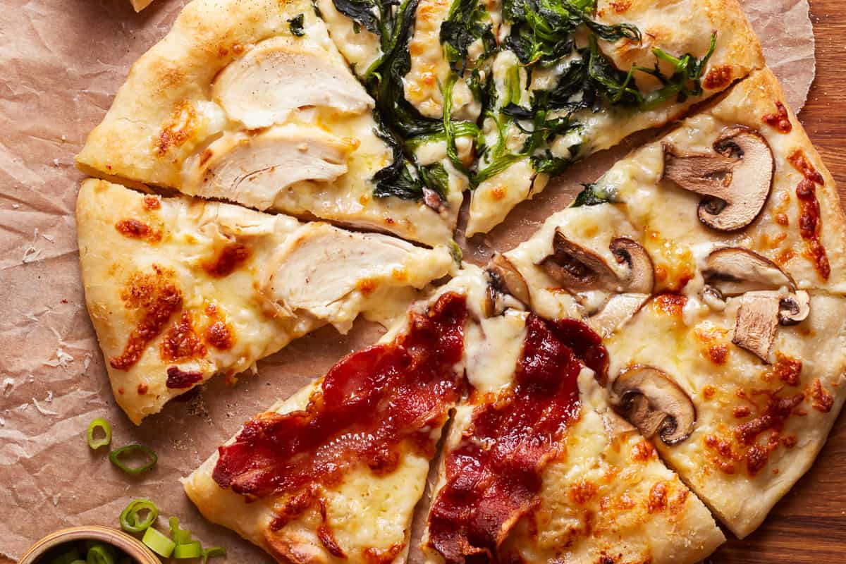 Alfredo sauce pizza, with different toppings on each slice: chicken, bacon, mushrooms, and spinach.