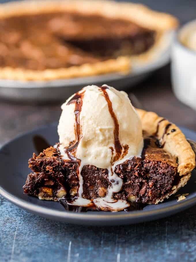A slice of chocolate pie topped with ice cream and chocolate sauce on a blue plate.