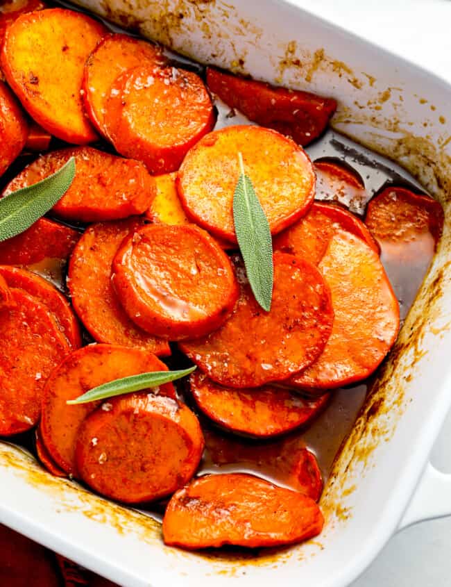 A white baking dish filled with sweet potatoes and sage.