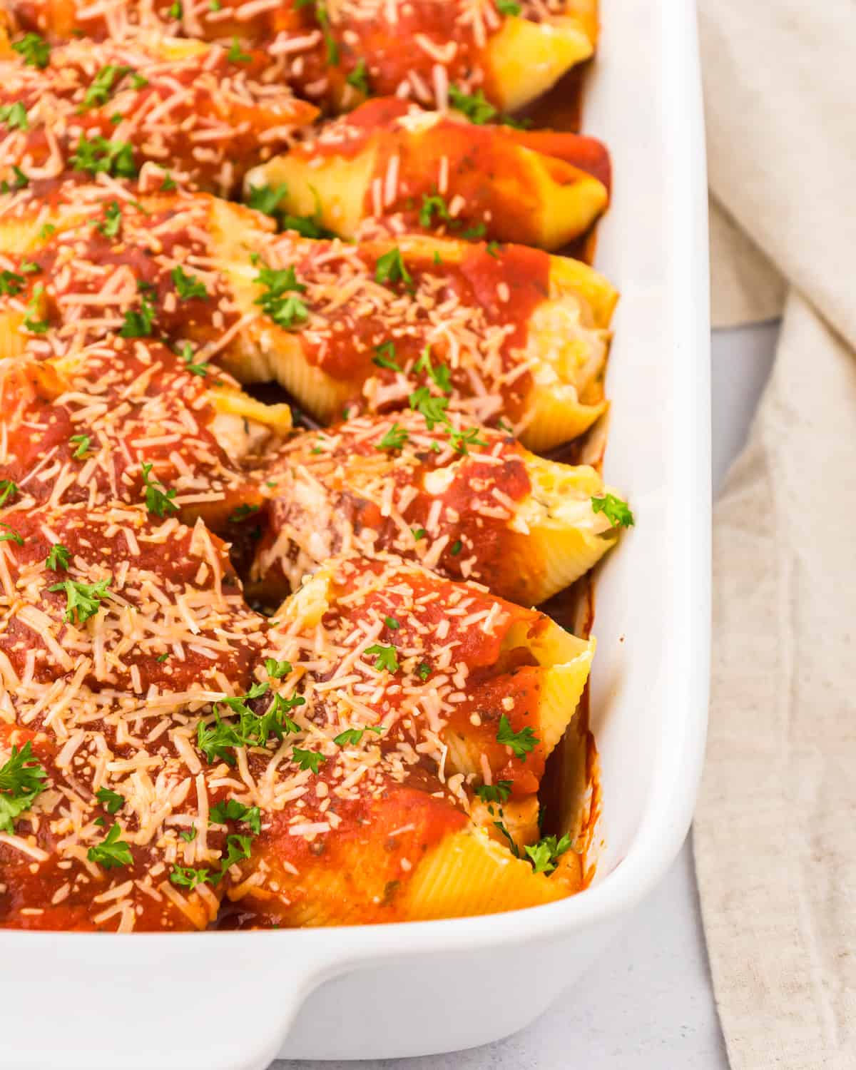 Chicken stuffed shells with marinara sauce and parmesan cheese in a white baking dish.