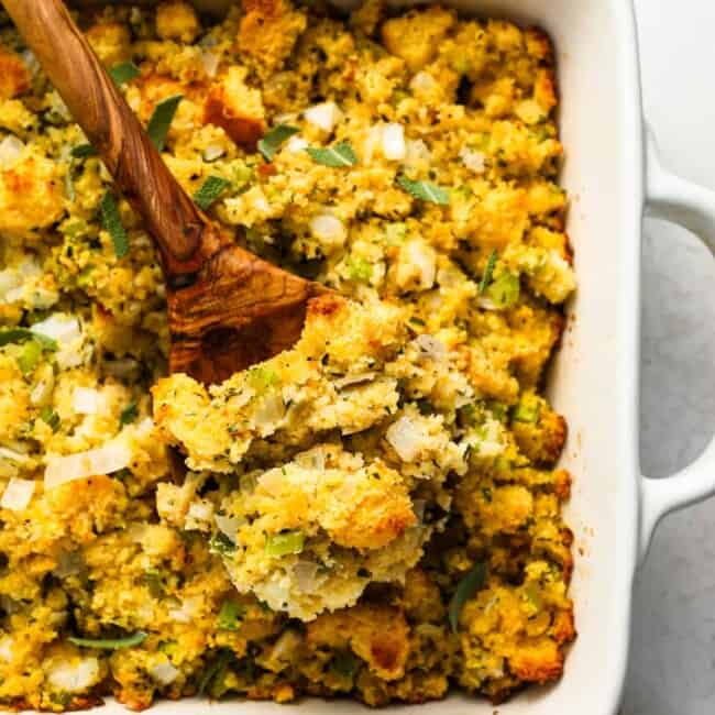 Cornbread stuffing in a white dish with a wooden spoon.